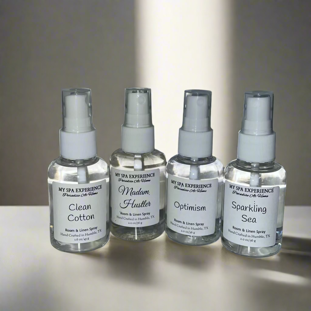 Four spray bottles labeled 'Clean Cotton', 'Madam Hustler', 'Optimism', and 'Sparkling Sea' on a tiled wall.